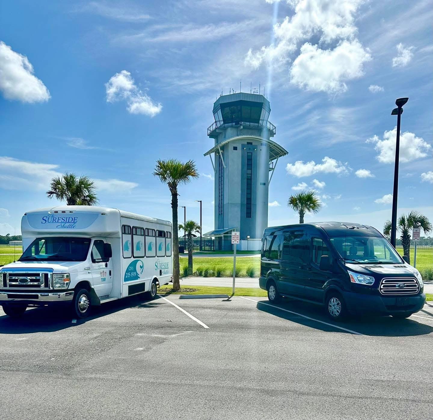 Two Shuttle Vehicles Parked in Front of an Airport Control Tower Under a Clear Blue Sky, Highlighting Transportation Services at the Airport.